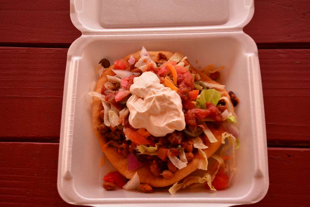 This is an absolutely mouthwatering photo of an Indian taco inside a styrofoam container.