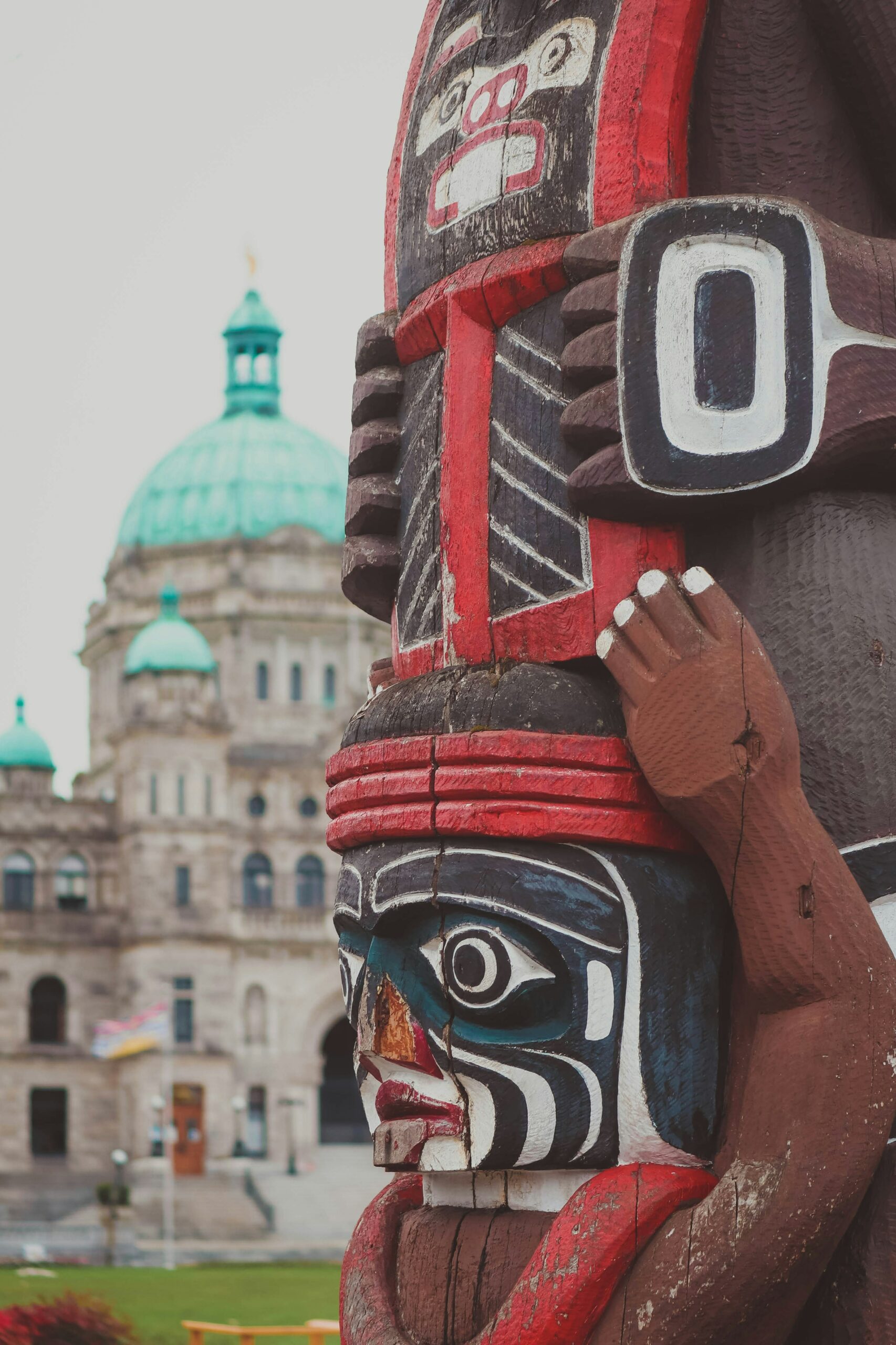 a photo of a Totem pole in Victoria, B.C., with the Legislative Assembly of British Columbia building in the background.