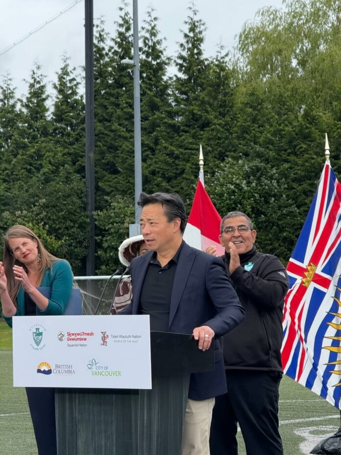 This is a photo of Ken Sim talking at a podium with two people next to him.