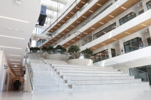 This is a photo of the SFU Surrey Engineering Building from the inside. There are numerous levels to the building, artificial trees, and a wide staircase in the photo.