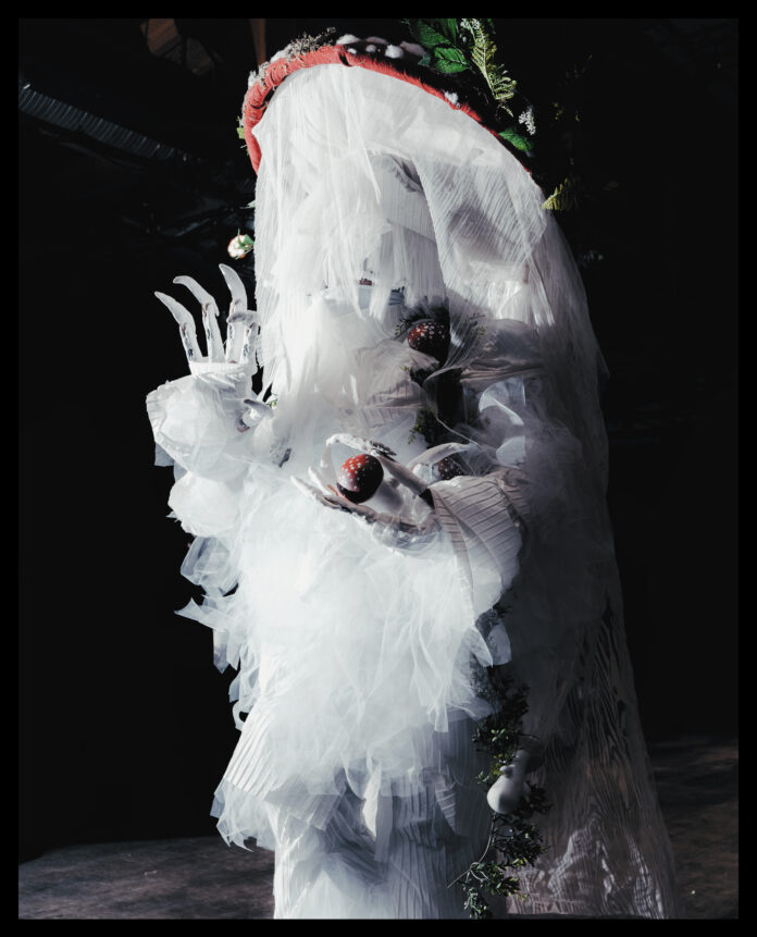 Ash Currie walking in the Bizarre category at the 2023 Supernatural kiki ball in Vancouver wearing an ethereal red and white mushroom costume. They’re holding a smaller red and white mushroom in their hand.