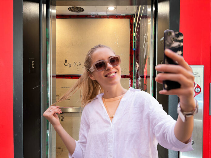 A girl with blonde hair taking a selfie in front of an elevator at SFU. The elevator is covered with cardboard inside.