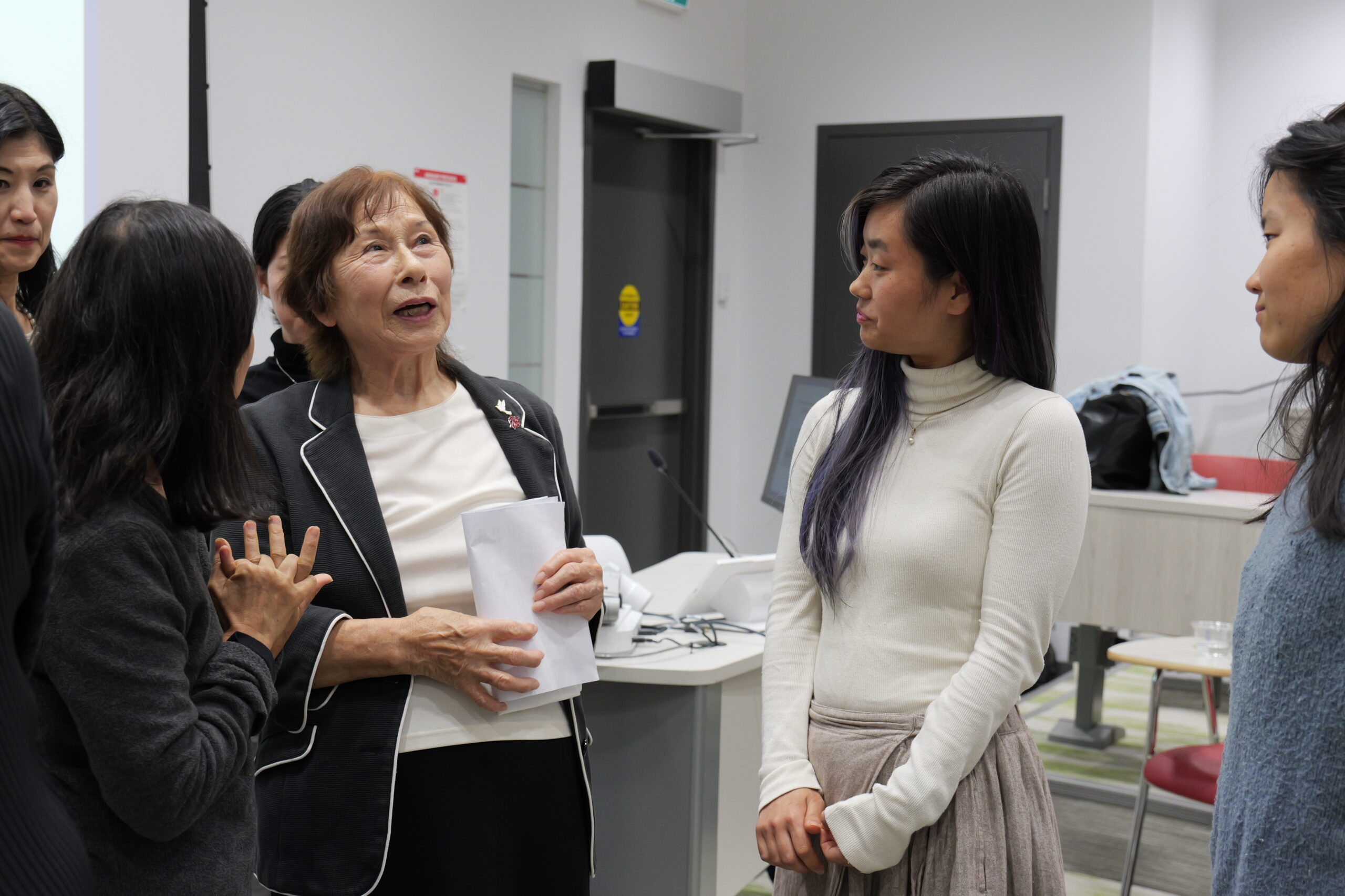 This is a photo of Kuramori Terumi speaking with some people at the front of the presentation room.