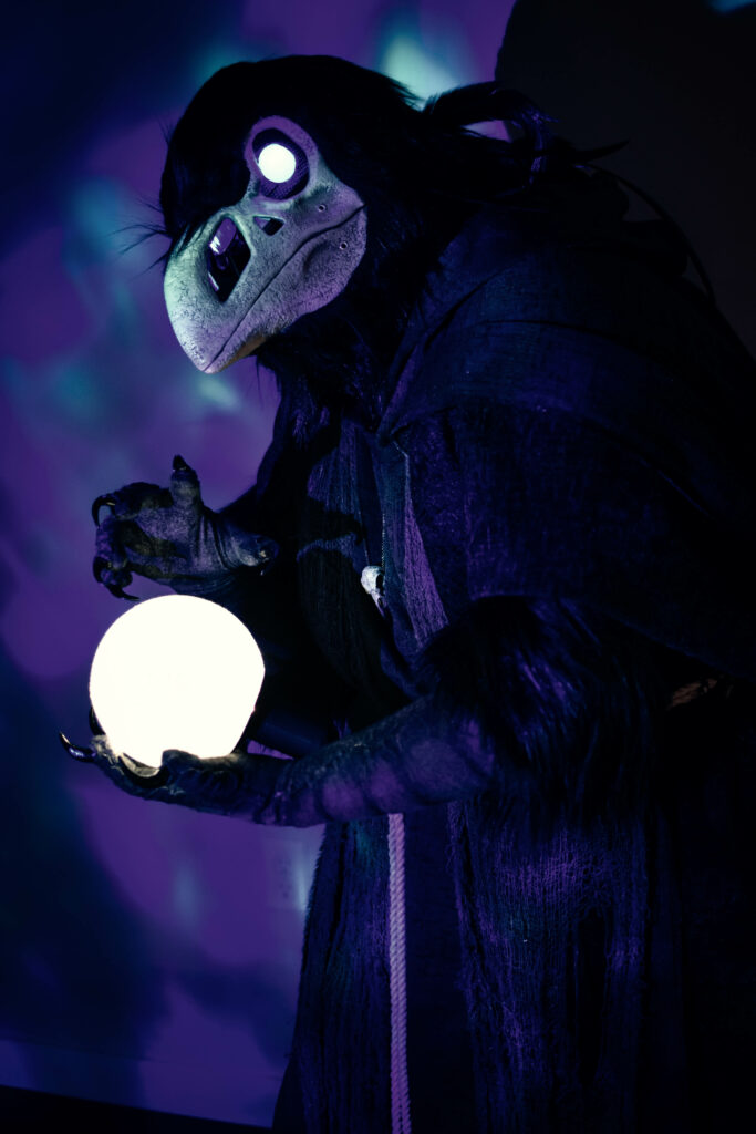 Ash Currie wearing a grim reaper raven costume. They are holding a glowing orb. This was their 2022 Halloween costume and the first costume they ever made.