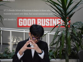 A student wearing business attire sitting next to a Beedie School of Business sign, contemplating.