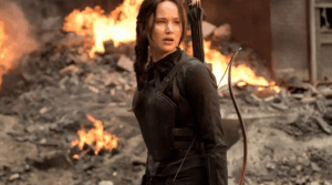 A girl standing with a bow and arrow behind a building on fire. It’s Katniss from Hunger Games.