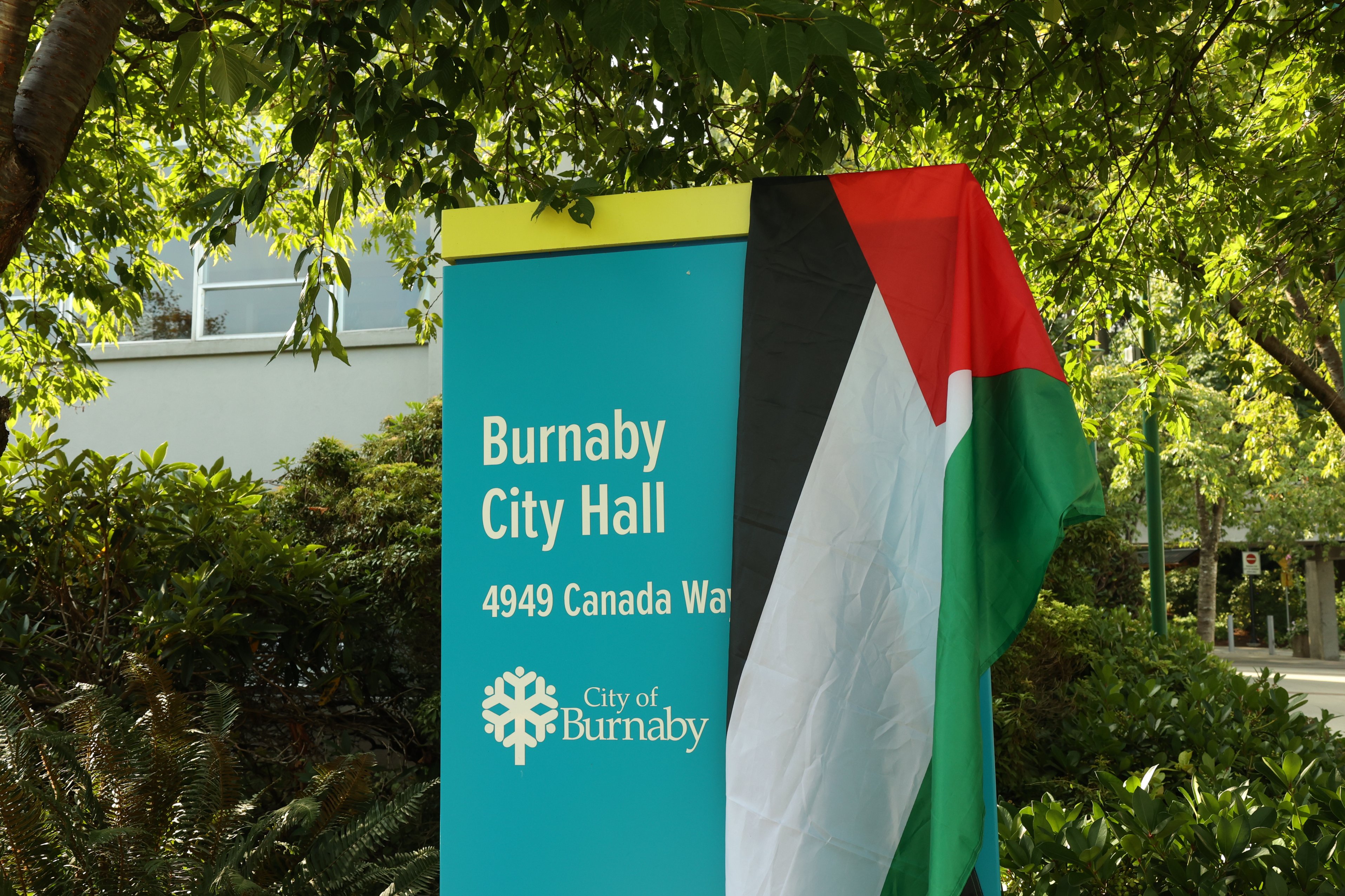 This is a photo of the entrance of Burnaby City Hall. The shot shows the part of the building that says “City Hall,” the entrance’s double doors, and a tree to the left of the entrance.