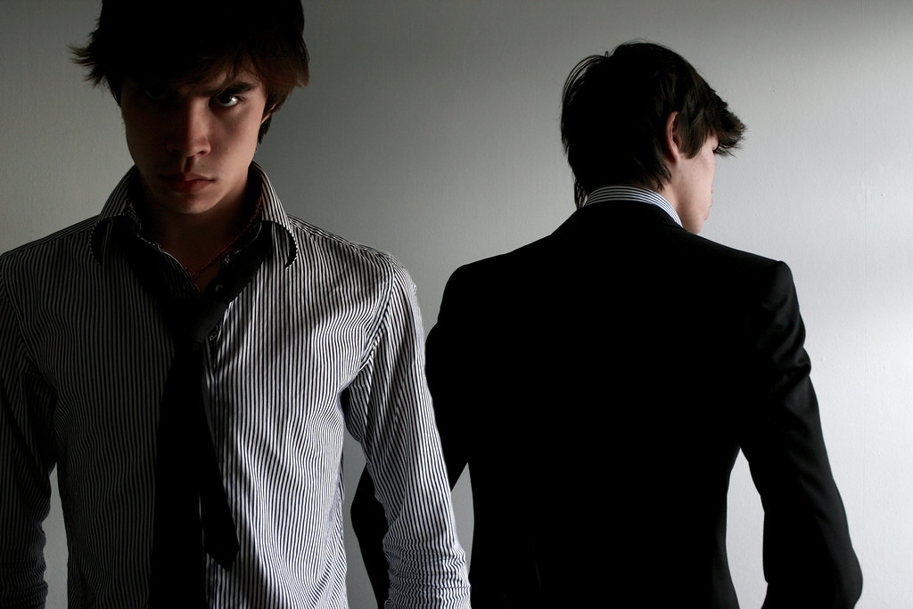 A man facing the camera, with a clone of his body facing away from the camera. It appears to be a clone of himself. Both are wearing business casual clothing.