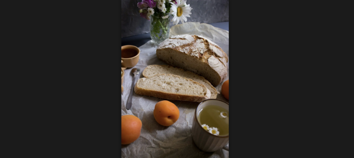 Half of a bread loaf, with two slices already cut-up next to it. There are three peaches and a tea mug in the scene. The picture is lit up with natural light.