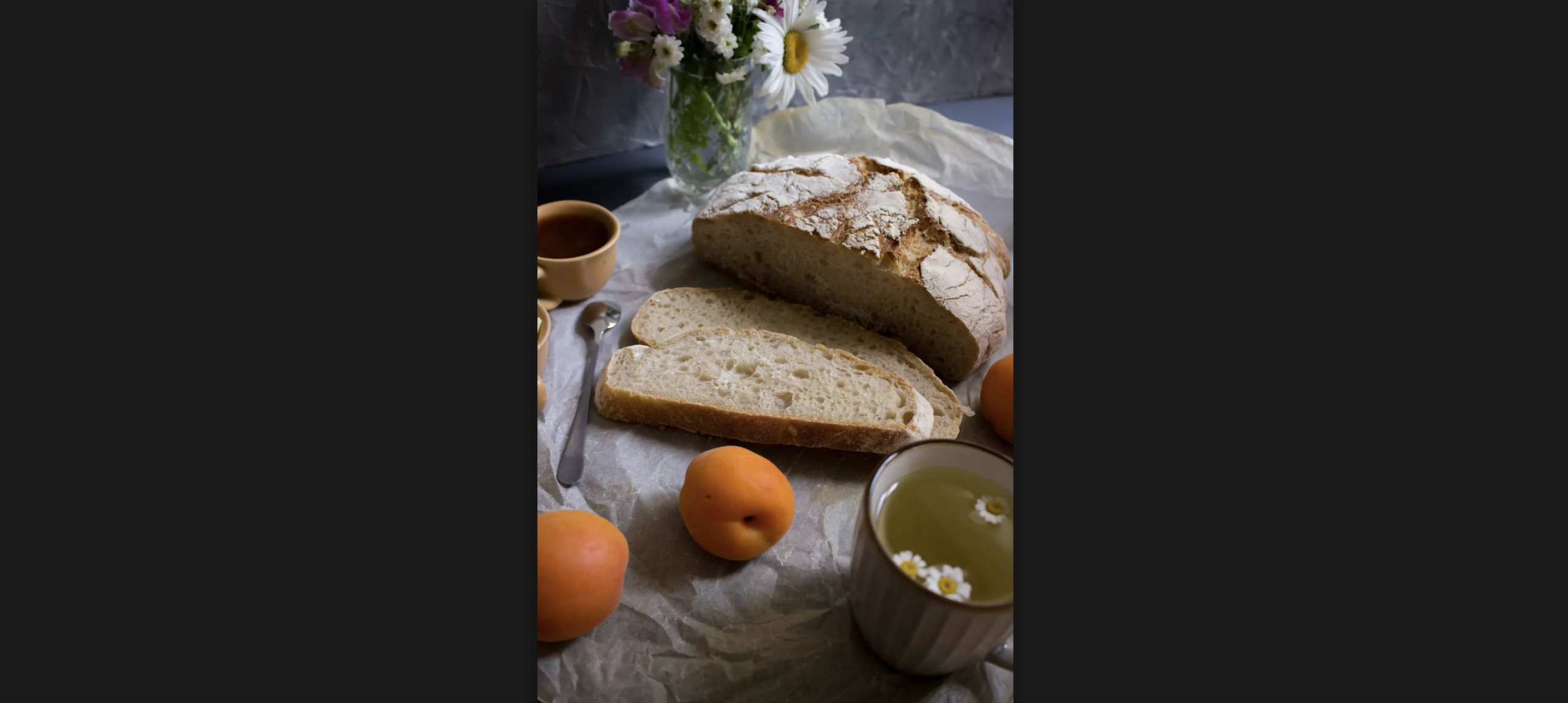 Half of a bread loaf, with two slices already cut-up next to it. There are three peaches and a tea mug in the scene. The picture is lit up with natural light.