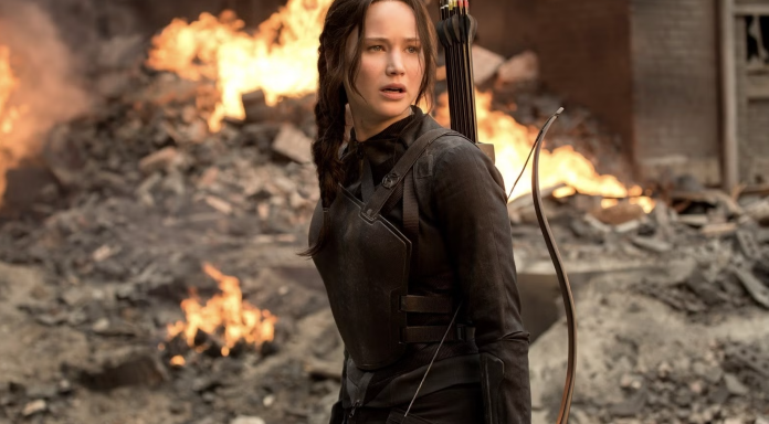 A girl standing with a bow and arrow behind a building on fire. It’s Katniss from Hunger Games.