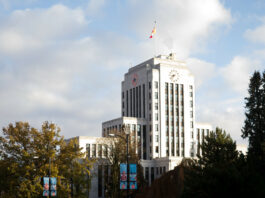 The outside of Vancouver City Hall is pictured on a bright day, with trees around it.