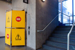 a photo of an out of order elevator on SFU’s Burnaby campus. The image shows a flight of stairs by the elevator. While the elevator itself is not visible due to a makeshift yellow, caution partition wall.