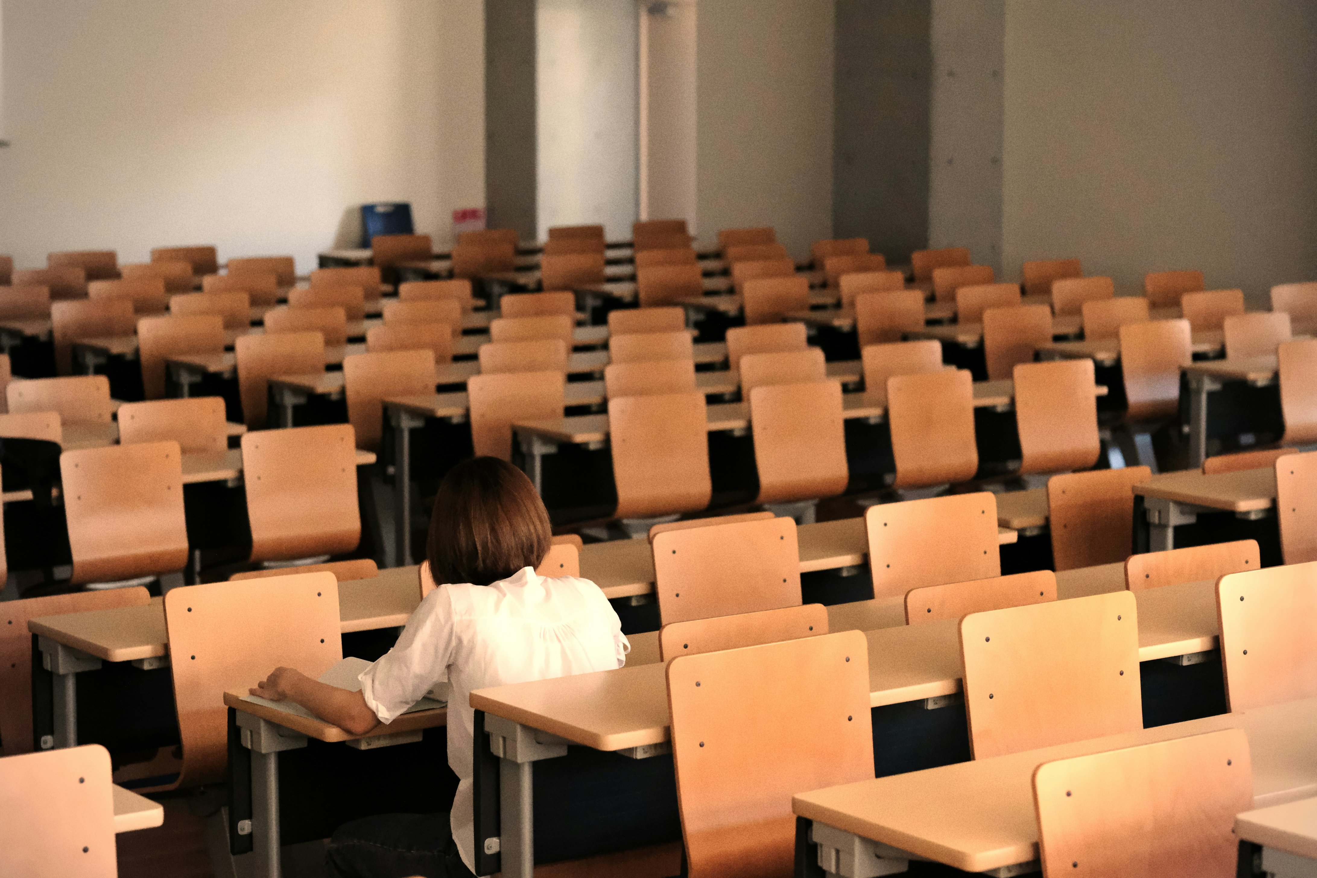 the image of an exam hall, filled with desks lined up throughout the hall. There’s one person sitting with their back towards the viewer.