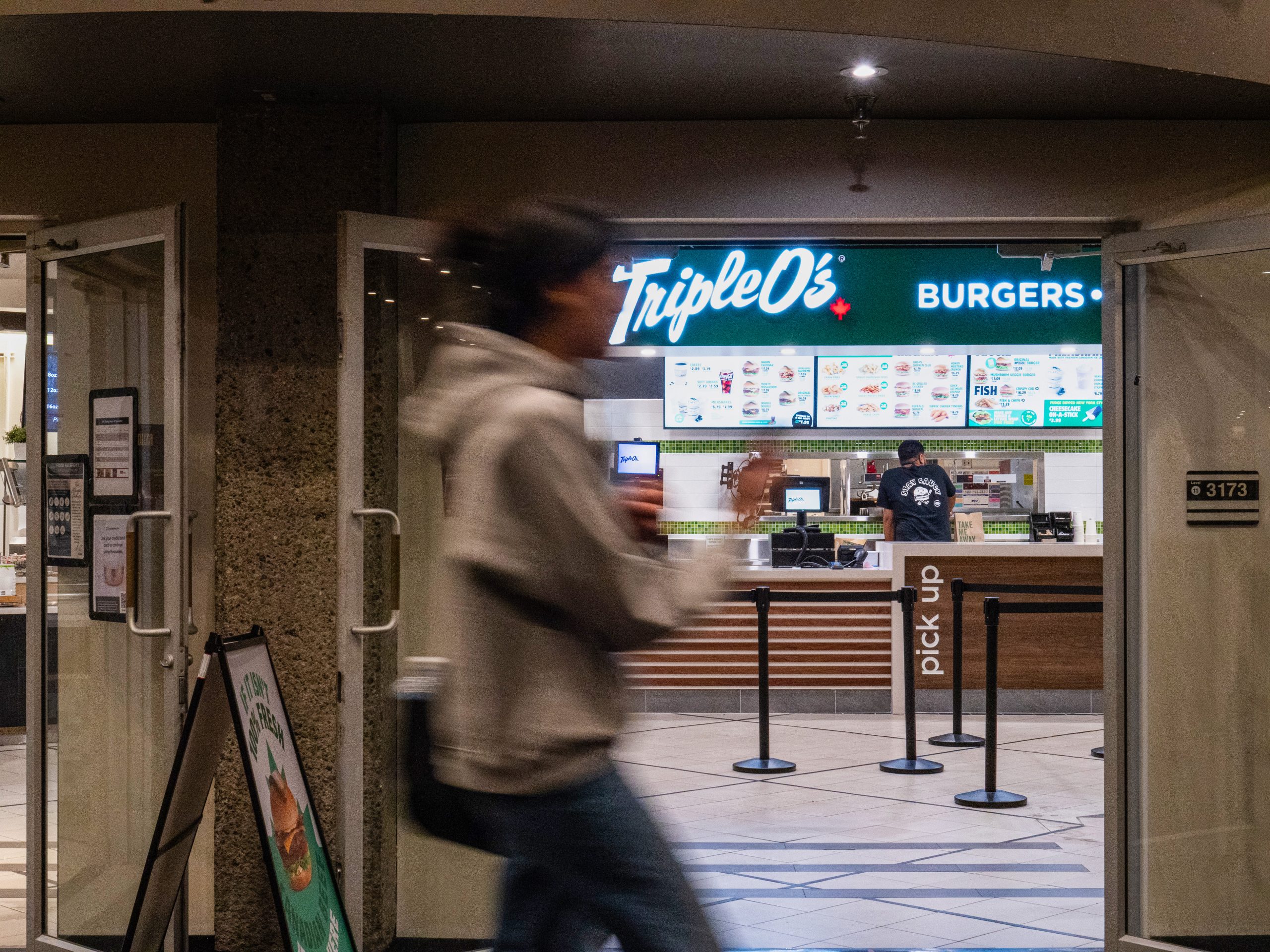 A photo of the newly opened Triple O’s on the Burnaby campus, in Mackenzie Cafe. There is a person walking in front of the restaurant, but they are blurry due to their movement.