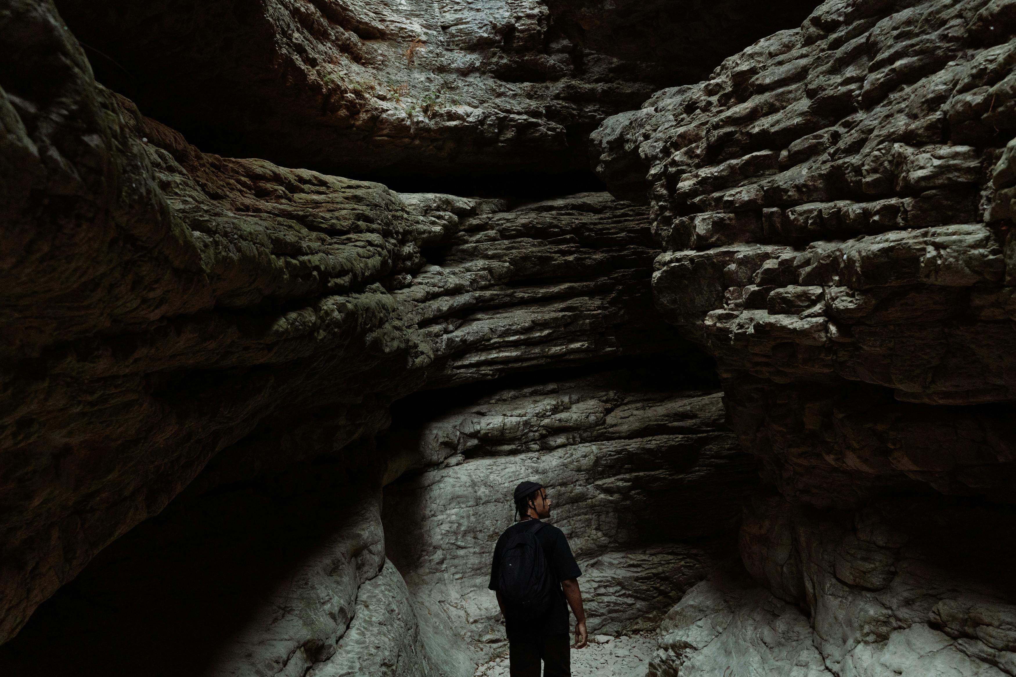 A man with a crossbody bag stands in a cave. He is looking to his right.