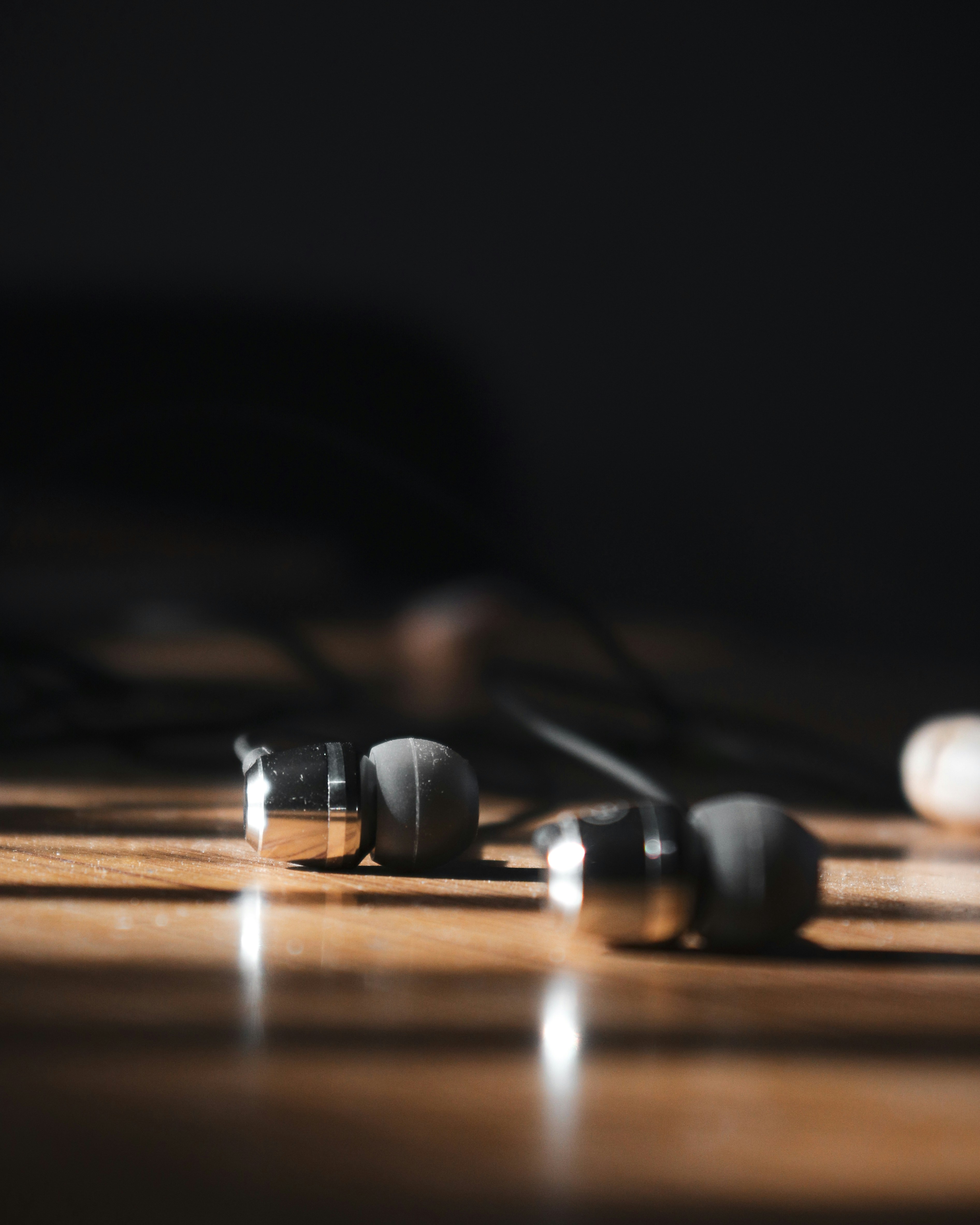 a close-up of black, wire, in-ear, headphones sitting on a wooden table.