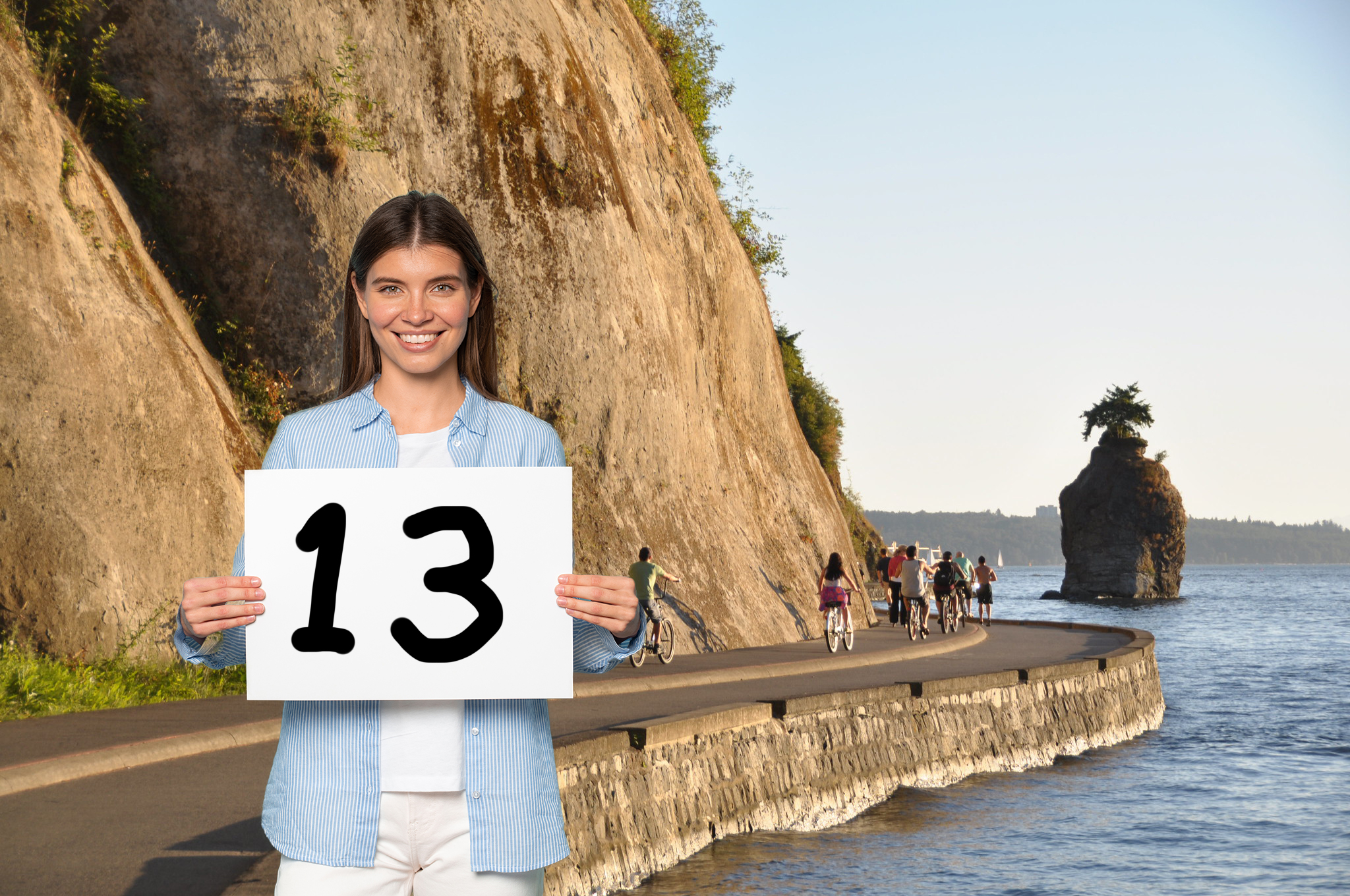 A girl wearing trendy clothes standing in front of the Sea Wall. She’s holding a paper with the number 13 on it.