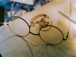 thin-framed round eyeglasses, on top of a paper. The Paper has a Hogwarts letterhead.