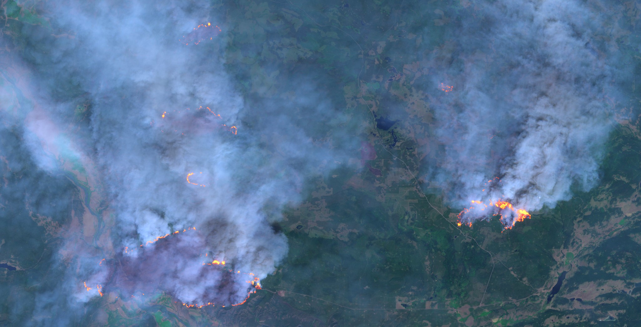 This is a photo of a recent wildfire in BC. It is a birds-eye view shot very high up in the air, where lots of smoke is coming from burning areas in the land.