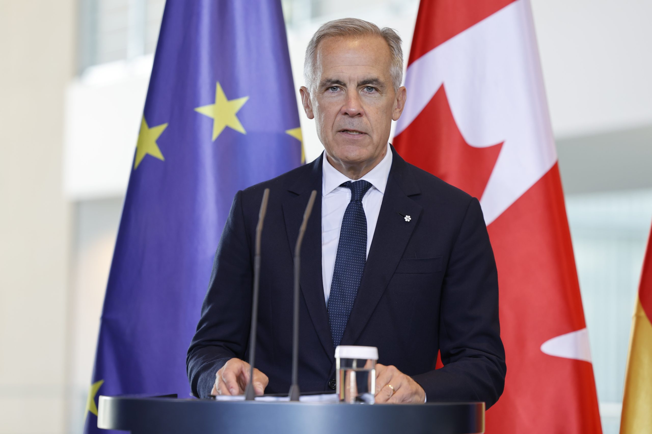 Mark Carney speaks behind a podium. The tone of the photo is serious.