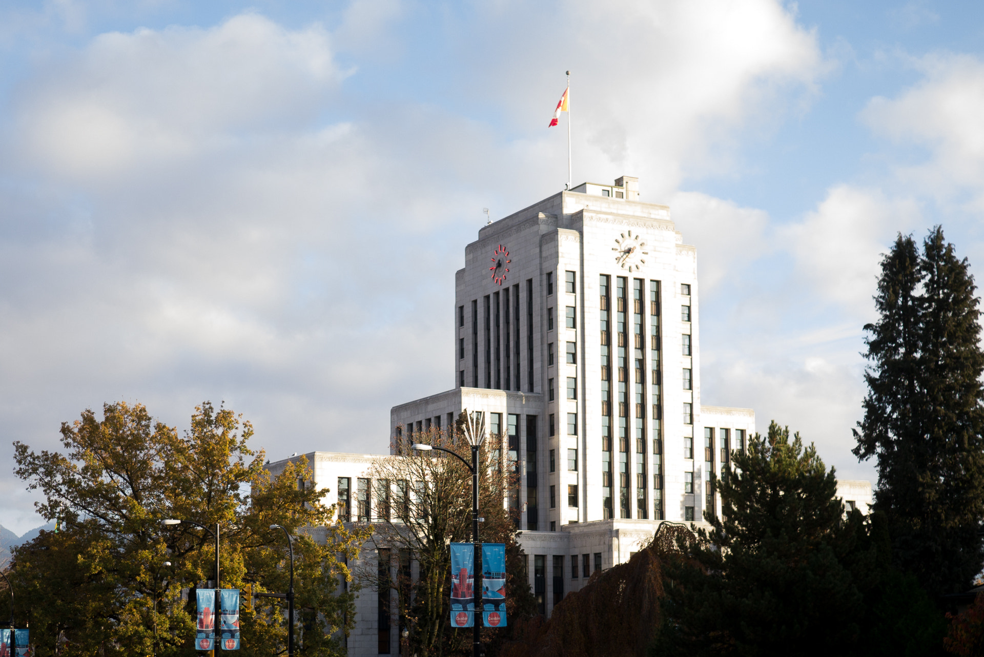 The outside of Vancouver City Hall is pictured on a bright day, with trees around it.