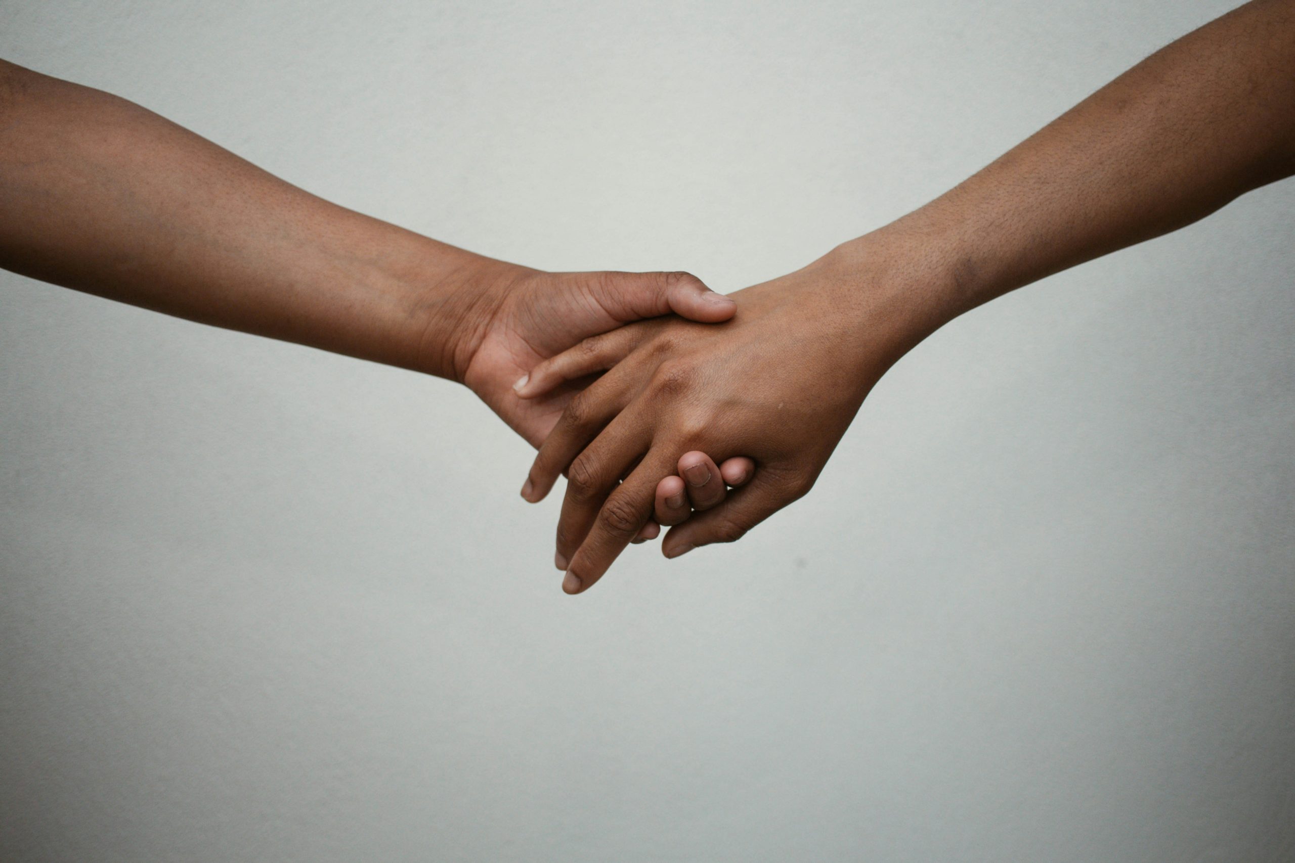Two people extend their arms from opposite sides of the photo and hold hands in the middle. The photo reflects the community support aspect of the study.