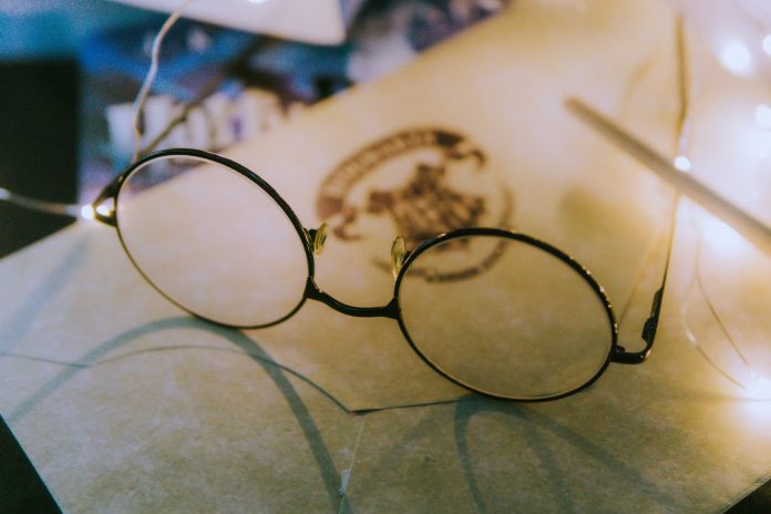 thin-framed round eyeglasses, on top of a paper. The Paper has a Hogwarts letterhead.