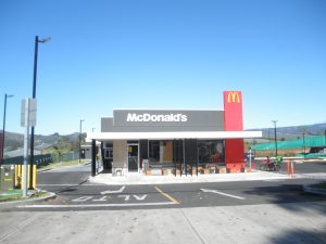 A sleek McDonalds stands solitarily within an expansive tropical Costa Rican landscape. A motorcycle is parked outside and the parking lot sits empty in front of the green, hilly distance.