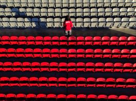 A student wearing an SFU sweatshirt turns their back to the camera as they stand in the middle of the SFU Stadium stands. The photo is solemn and expresses loss, with the key colour being red for SFU’s Red Leafs.