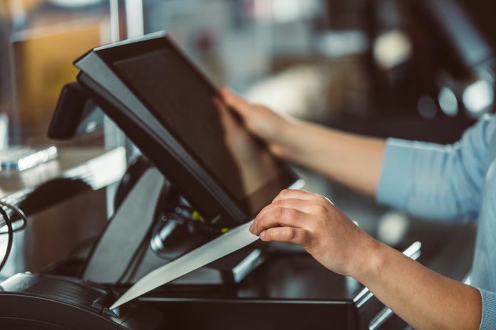 The photo of a cashier’s hands, near the cash till, as they are printing a receipt.