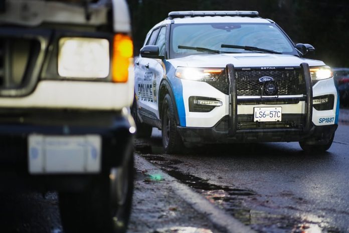 A Surrey Police car pulls up beside a white car. The front view of both cars is shown, with the police car’s lights flashing brightly.