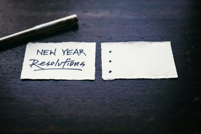 a set of two small white notes, one has “New Year resolutions” written on it, and the other has three bullet points that are yet to be added. There’s a pen right beside the notes.