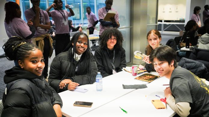 Five grade 8–12 students sit around a table and smile for the camera as they participate in the 2025 Blackathon at Microsoft Offices.