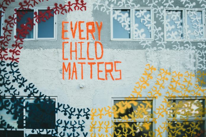 A wall of “Every Child Matters” and little stick-figure children holding hands in circles is pictured.