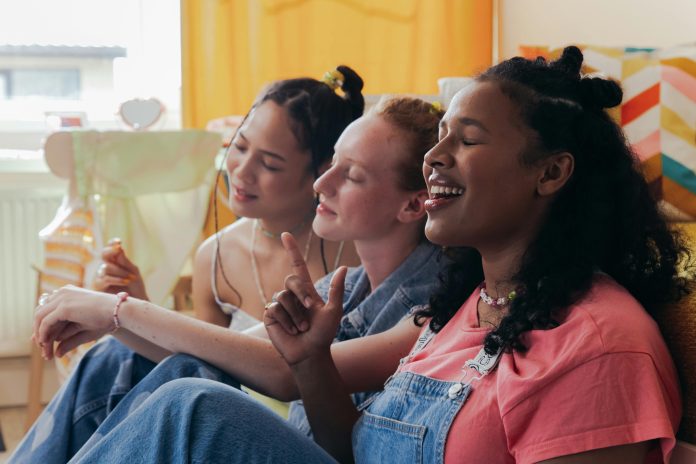 Three women sitting together in a bedroom laughing.