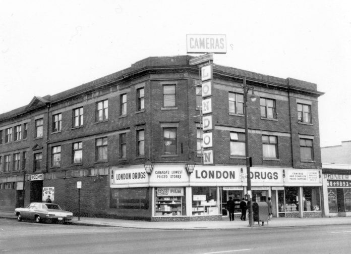 A black and white photograph of the London Drugs in Hogan’s Alley, 1968, is pictured. There are two floors above the store of apartments, and this building sits at the corner of the streets its on.