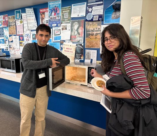 The rivalry between The Ubyssey and The Peak Two humour editors stand next to a microwave with spaghetti spilled all over the inside.