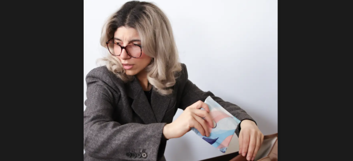 a woman takes out a pad out of her bag in the office. She is visibly self-conscious, and is checking to see if she is seen by others.
