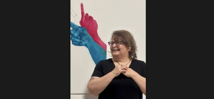 A photo of Laurie Landry with one of her artwork in the background