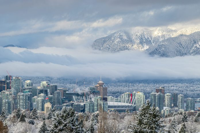 A snowy City of Vancouver and the surrounding mountains are pictured from afar.