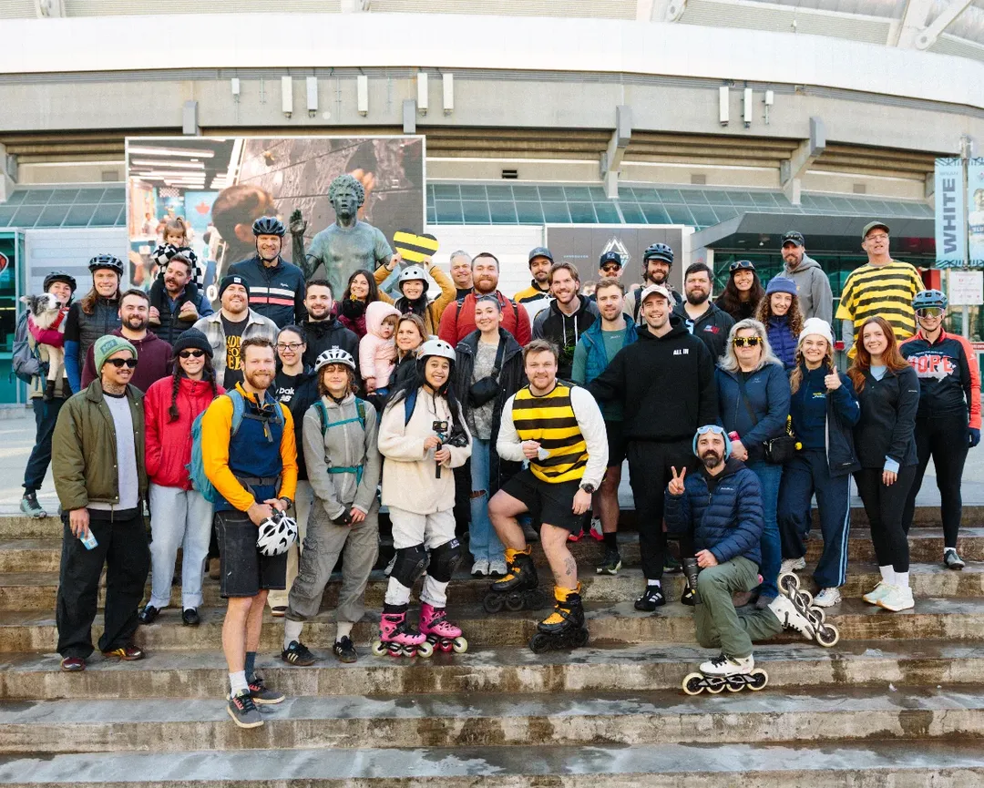 Zach smiles for the camera in a bee-inspired striped shirt alongside a crowd of supporters and the Terry Fox statue in front of BC Place.