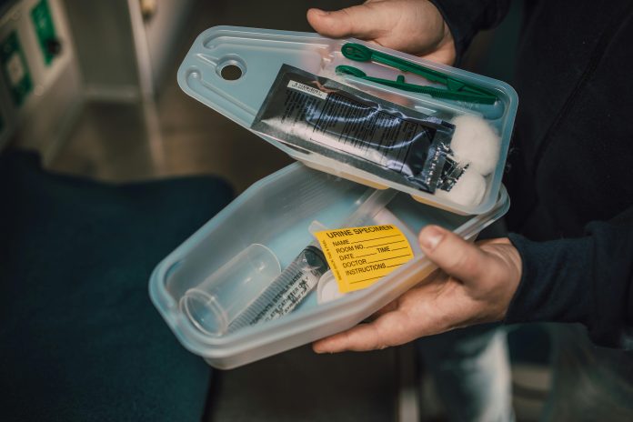 Image of someone holding a small open portable medical kit containing cotton swabs, tongs, and a catheter, among other items
