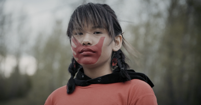 A scene from I Am Gitxsan showing a person with a red hand on their mouth