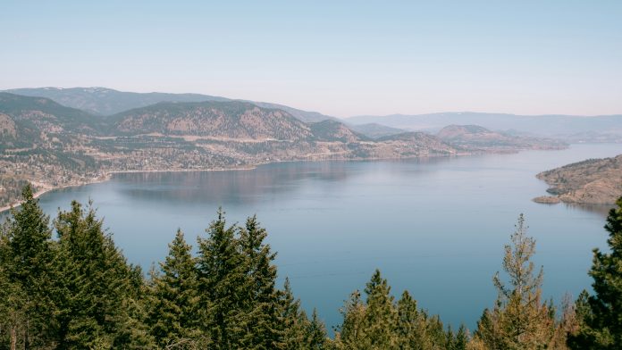 Scenic image of Okanagan lake, with trees and mountains surrounding the water