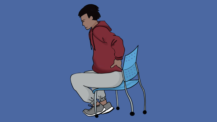 A student wearing a red hoodie with a pained lower back while sitting on an uncomfortable plastic chair