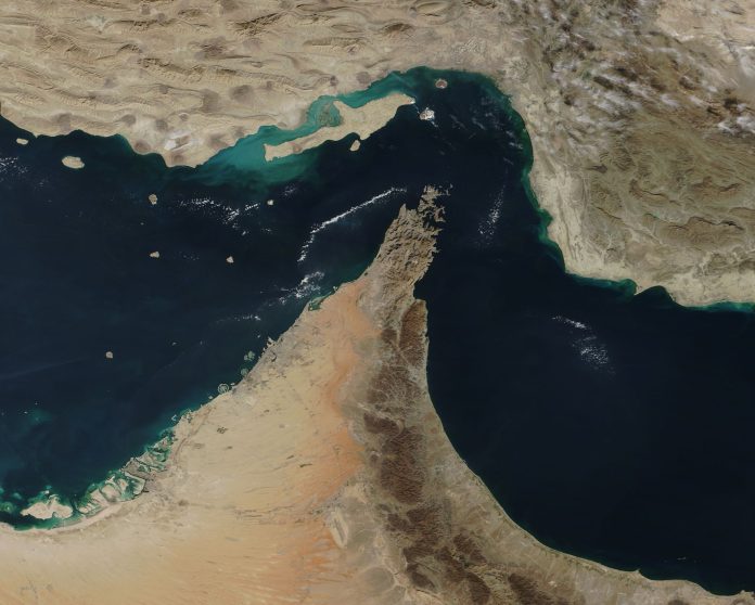 Aerial view image of Strait of Hormutz in colour. The ocean is deep blue, and turquoise near land. Land is pictured in tan, brown, and muddy red.