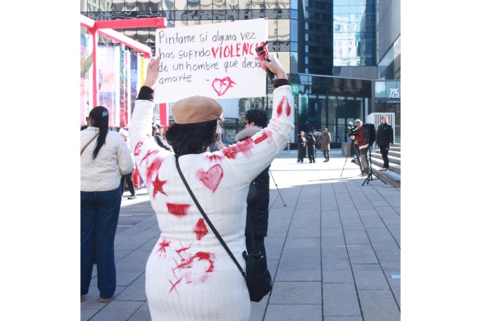 Woman activist holding a sign, covered in paint by other women who've experienced violence at the hands of male partners at the Vancouver International Women's Day March