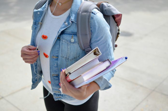 A photo of a student carrying books in one arm, adjusting their earphones.