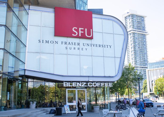 Photo of SFU Surrey campus sign embossed on Surrey building. Text reads “SFU” in white text, with red box background. On glass panels below, text reads “SIMON FRASER UNIVERSITY” and “SURREY”